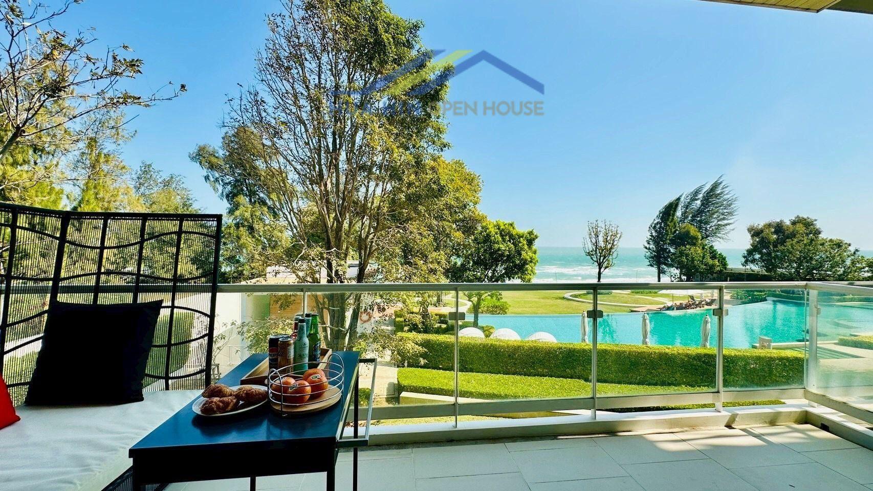 Spacious balcony with a view of the pool and beachfront, featuring a seating area and refreshments.