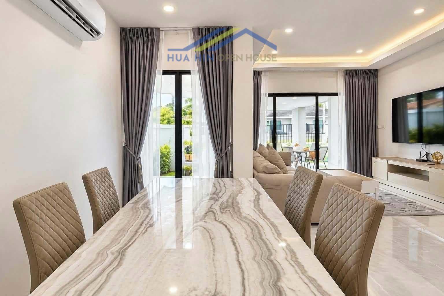 Modern dining area with a marble table, stylish chairs, and large windows leading to outdoor seating in a pool villa.