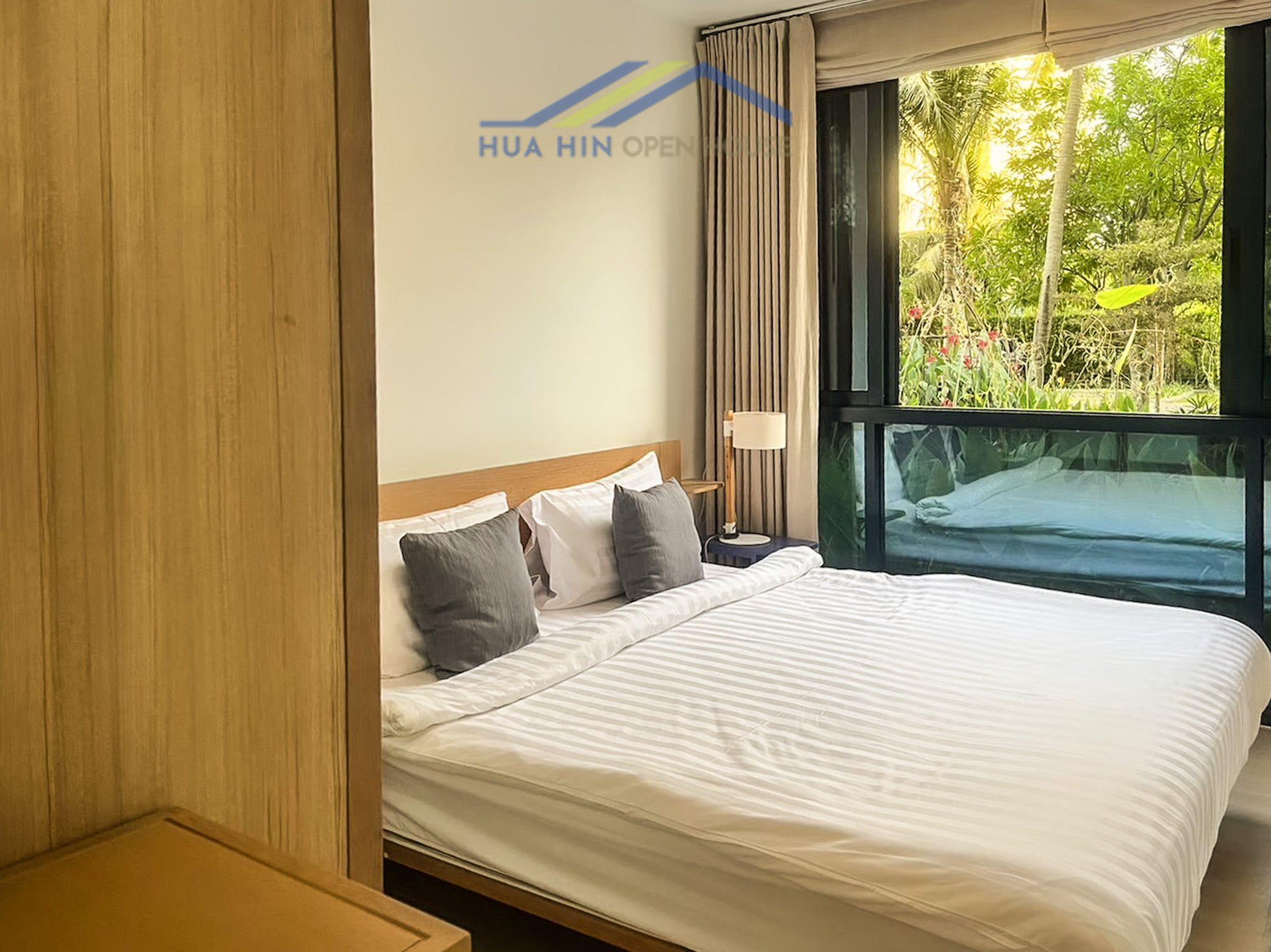 Bright bedroom featuring a king-sized bed, modern decor, and large windows with views of a lush garden.