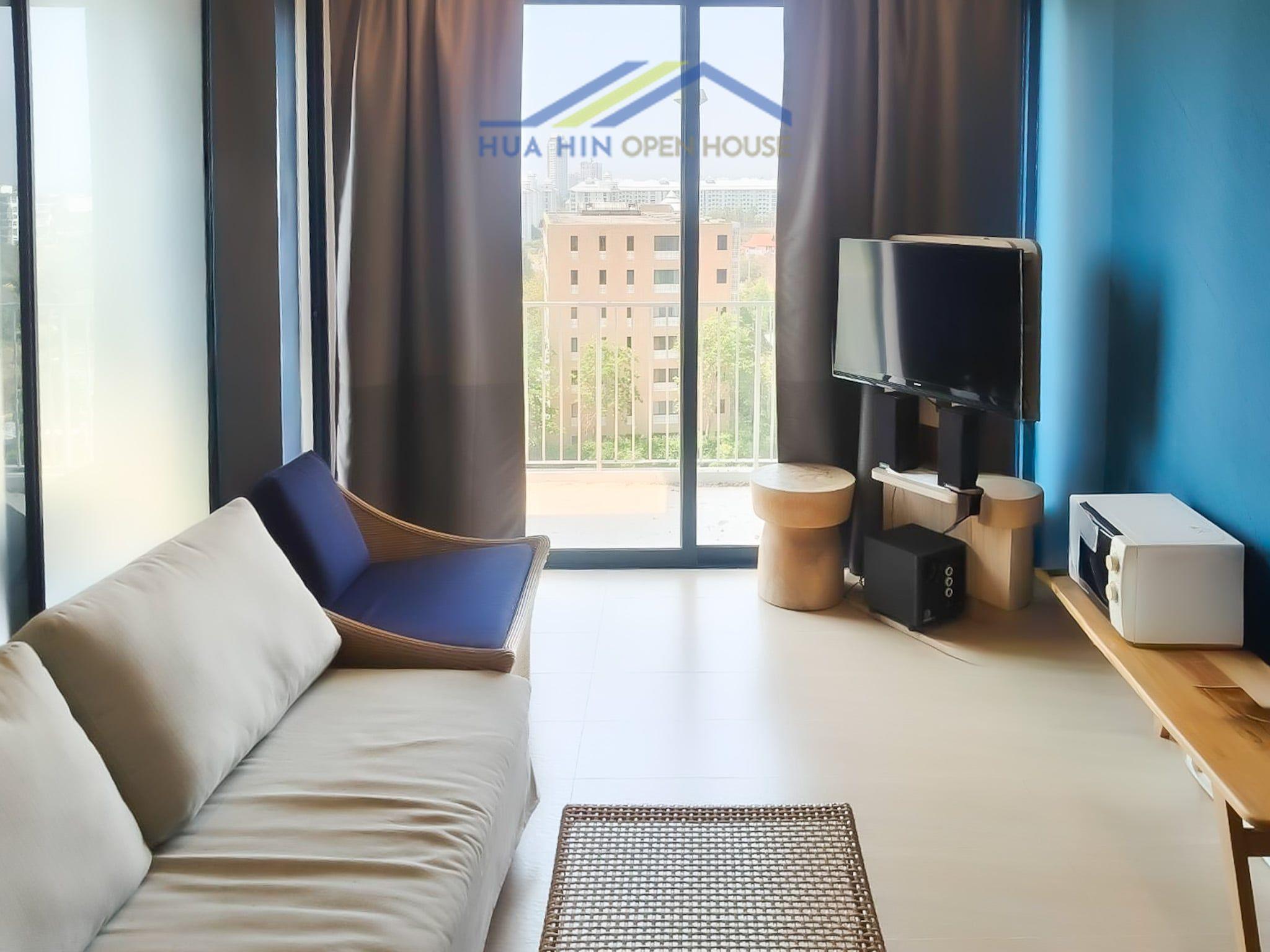 Modern living area in a beachfront condo, featuring a sofa, TV, and large windows with natural light.