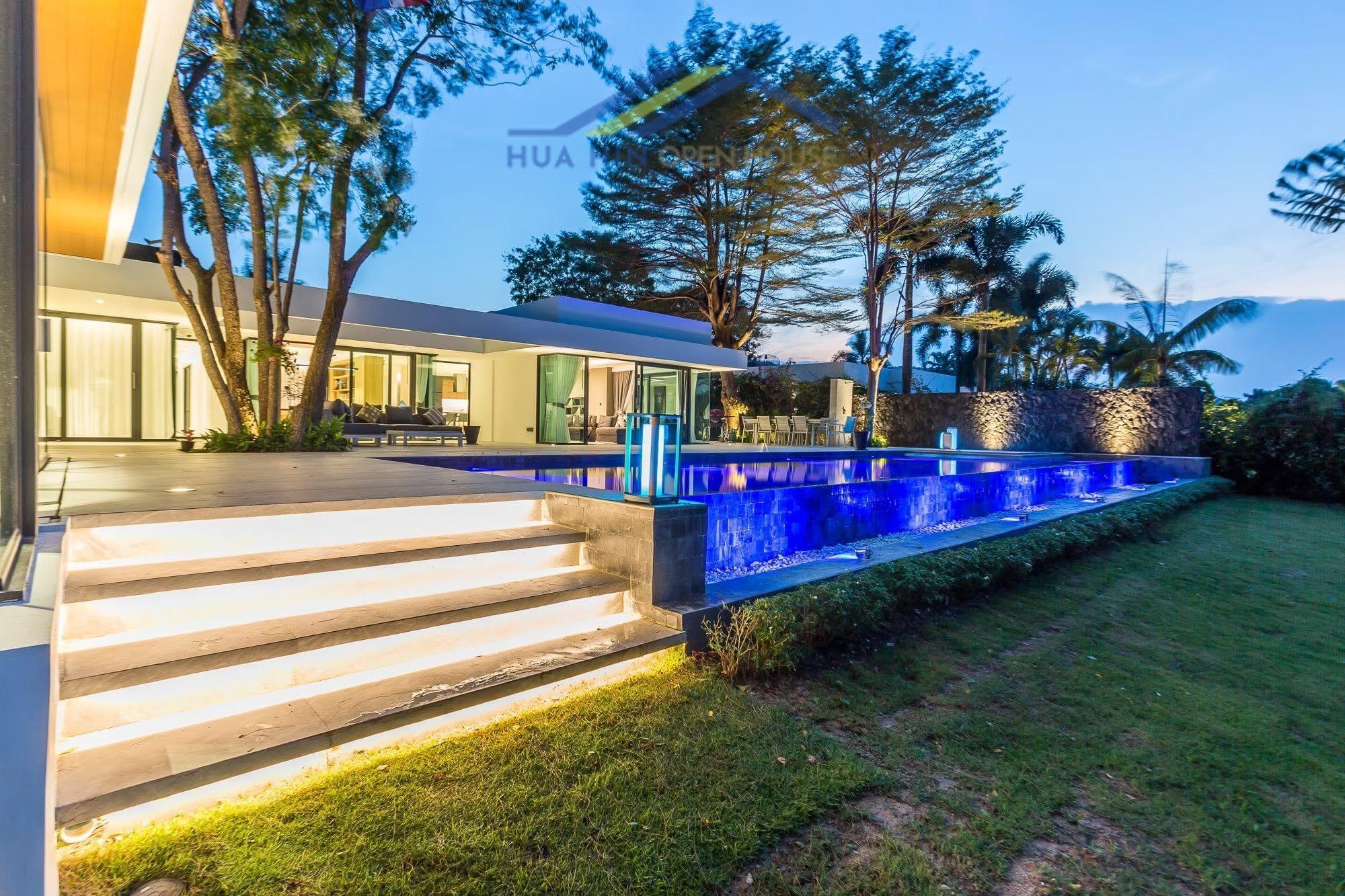 Modern luxury villa with illuminated pool, landscaped garden, and outdoor seating at Palm Hills Golf Course, Hua Hin.