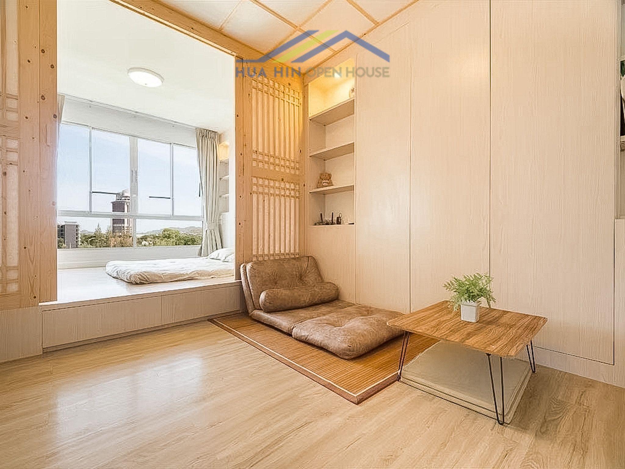 Cozy bedroom in a Japanese-inspired condo, featuring a sitting area, wooden accents, and large windows with natural light.