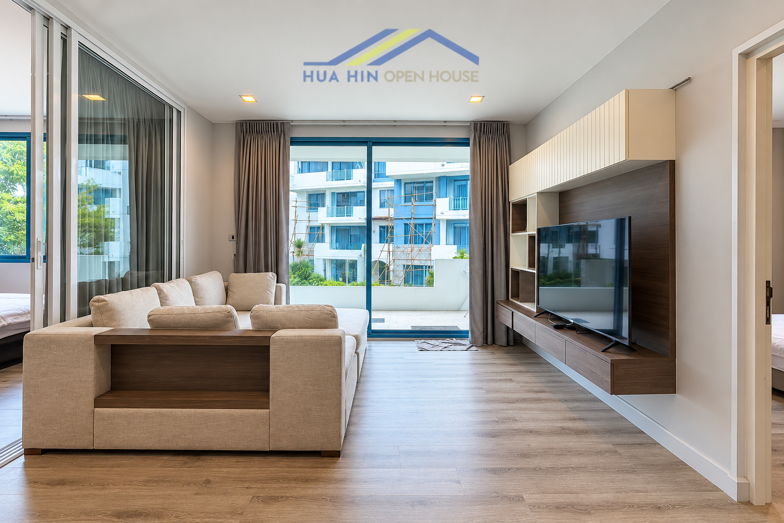 Spacious living area with a modern sofa, wall-mounted TV, and large windows overlooking the outdoor space.