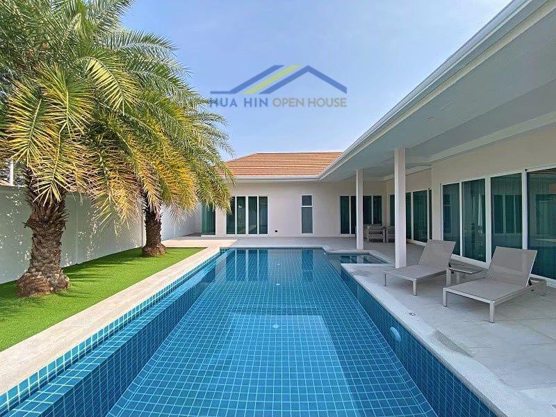 Modern pool villa with a spacious outdoor area, palm trees, and lounge chairs beside a shimmering blue pool in Hua Hin.