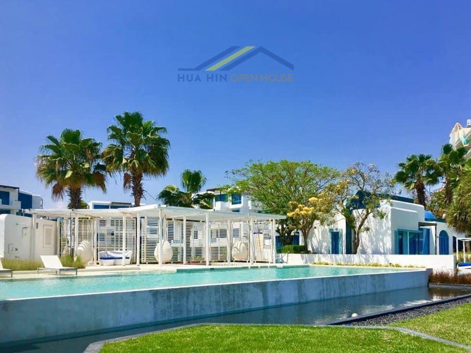 Tropical pool area with palm trees, sun loungers, and modern architecture at The Crest Santora, Hua Hin.