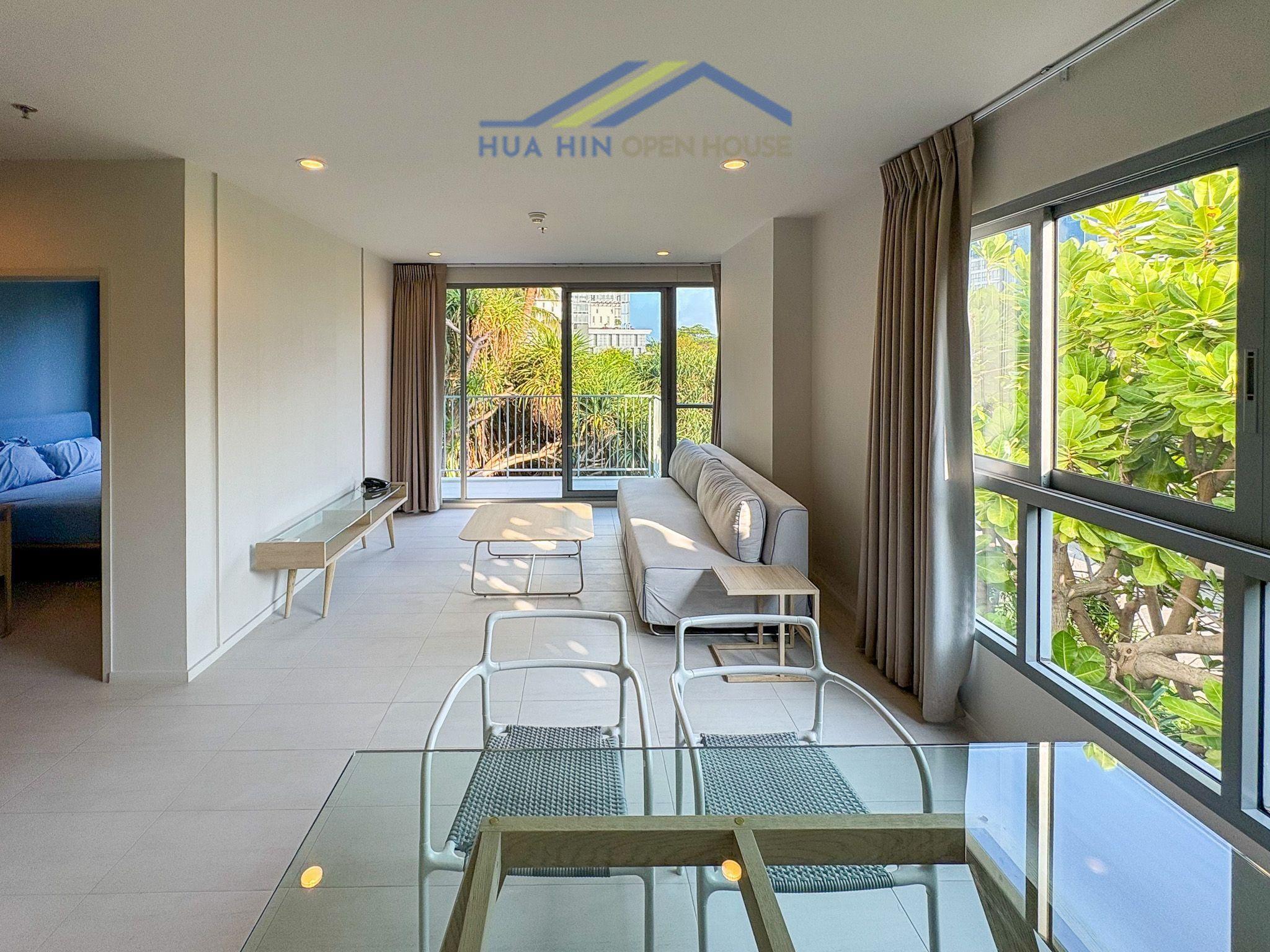 Spacious corner unit living area with modern furnishings, large windows, and views of greenery in BLU Cha-Am condo.