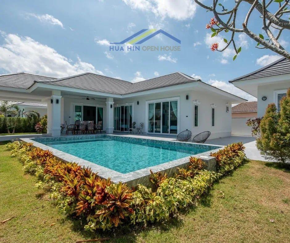 Modern villa in Hua Hin with a private swimming pool, lush gardens, and outdoor seating areas under a bright blue sky.